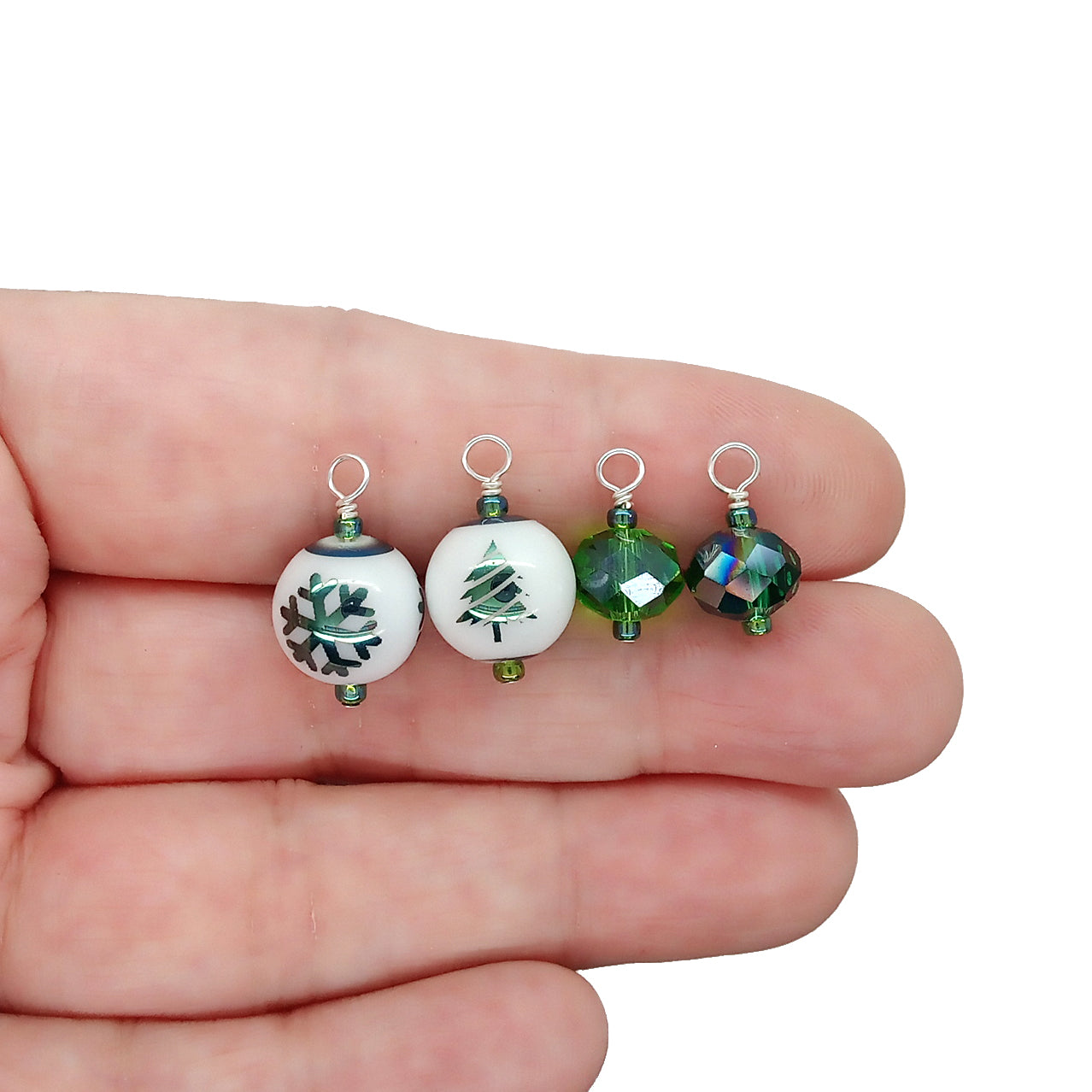 Four small Christmas green bead dangles held in a hand.