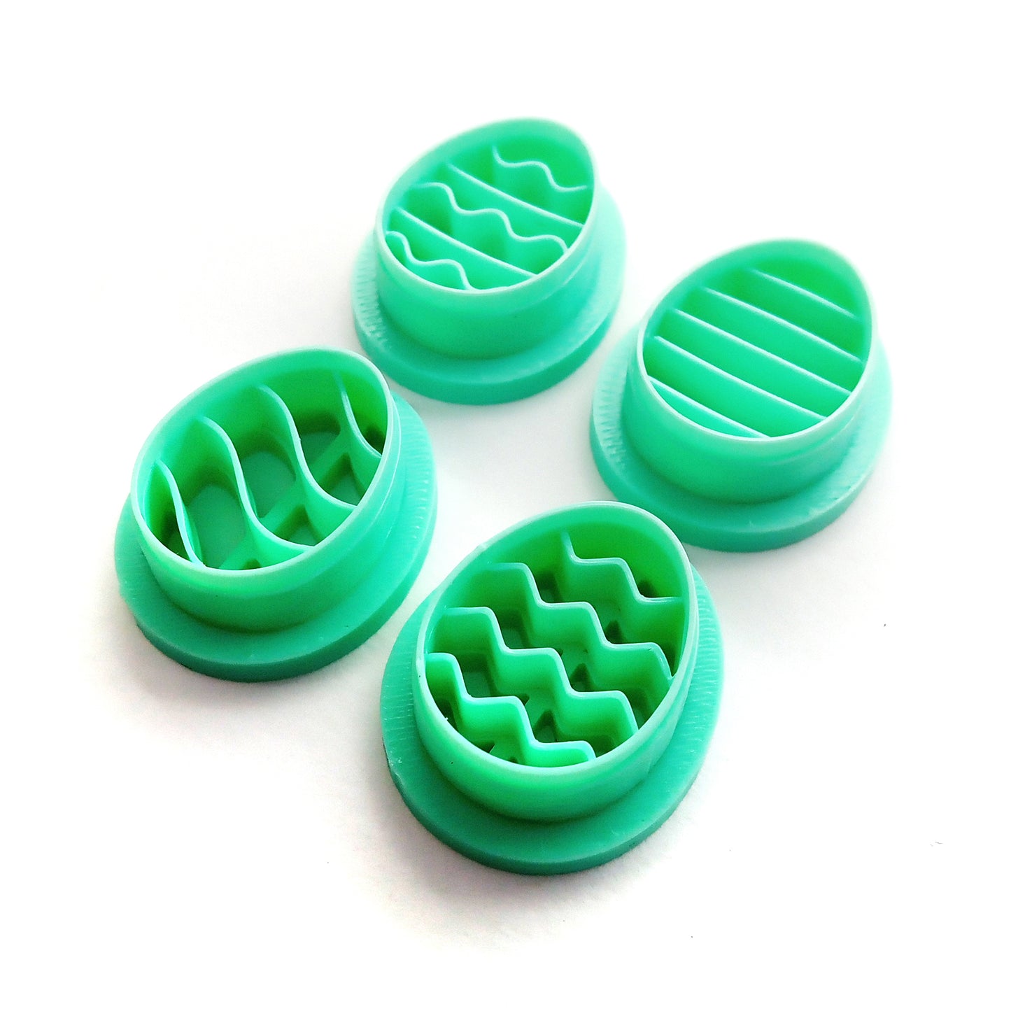 Four green egg-shaped clay cutters with different patterns on a white background