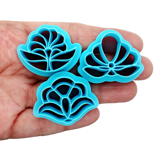 Three blue floral clay cutters held in a hand against a white background