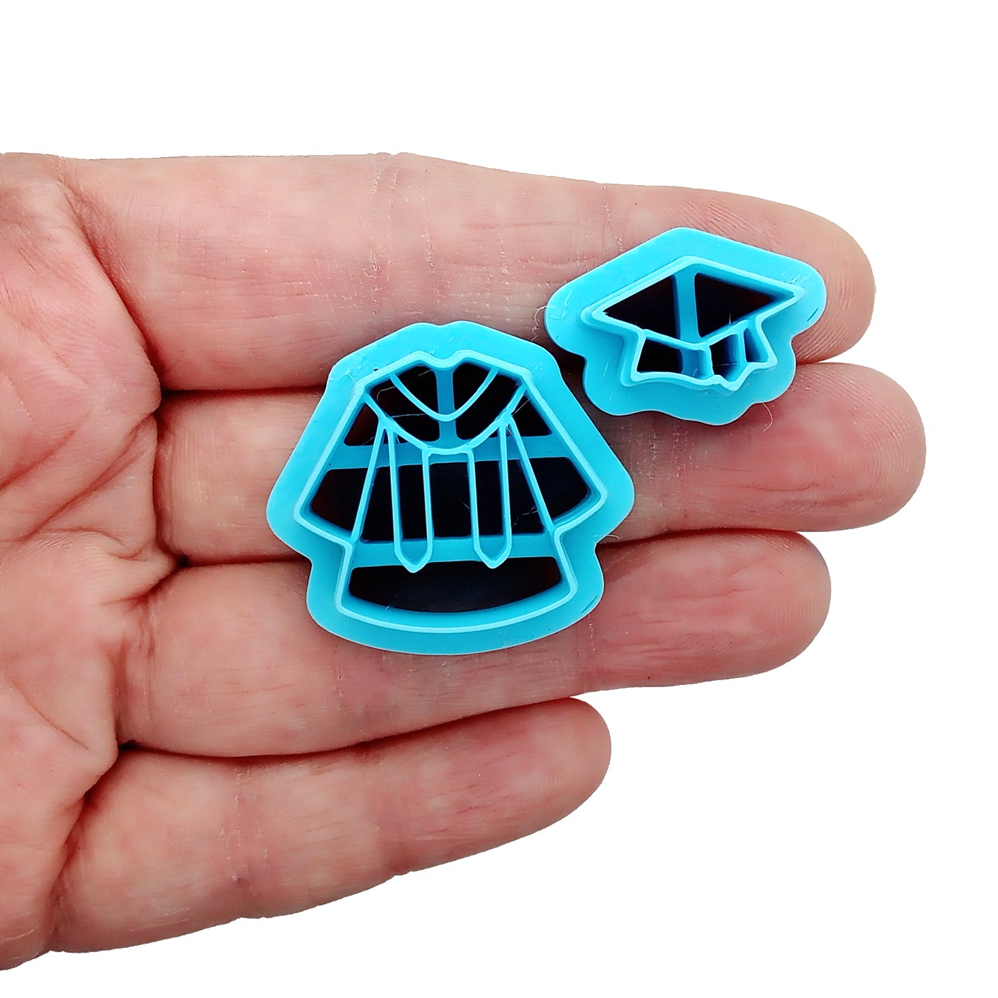 Two blue clay cutters shaped like graduation caps and gowns in a hand