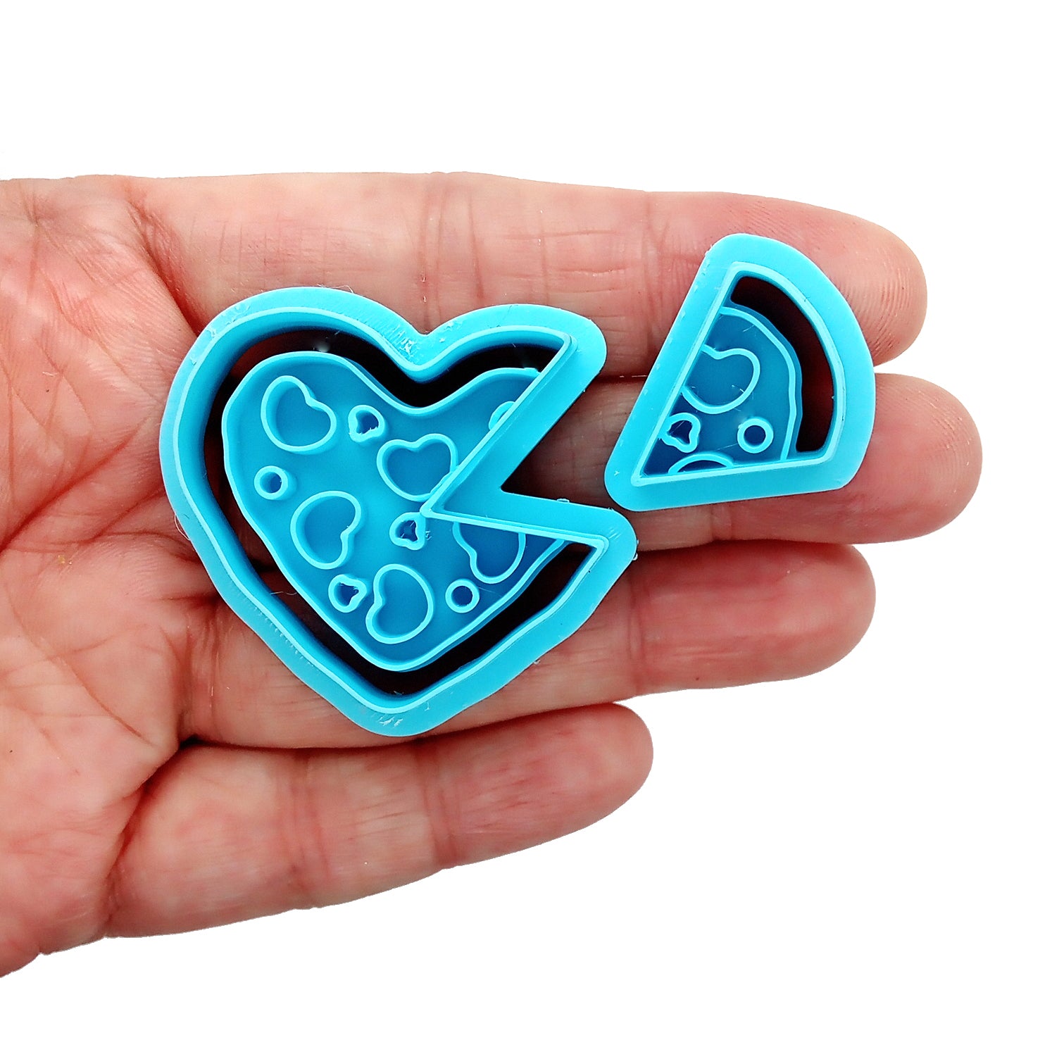Blue clay cutters shaped like a heart and a slice of pizza held in a hand on a white background