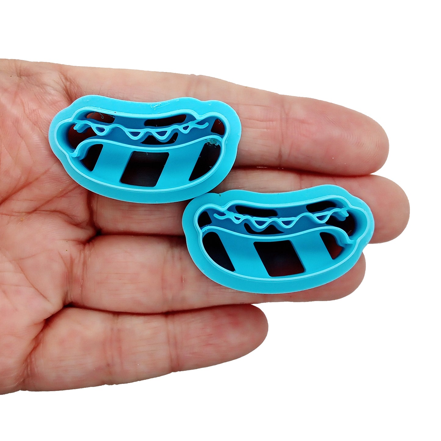 Two hot dog clay cutters in a hand on a white background.