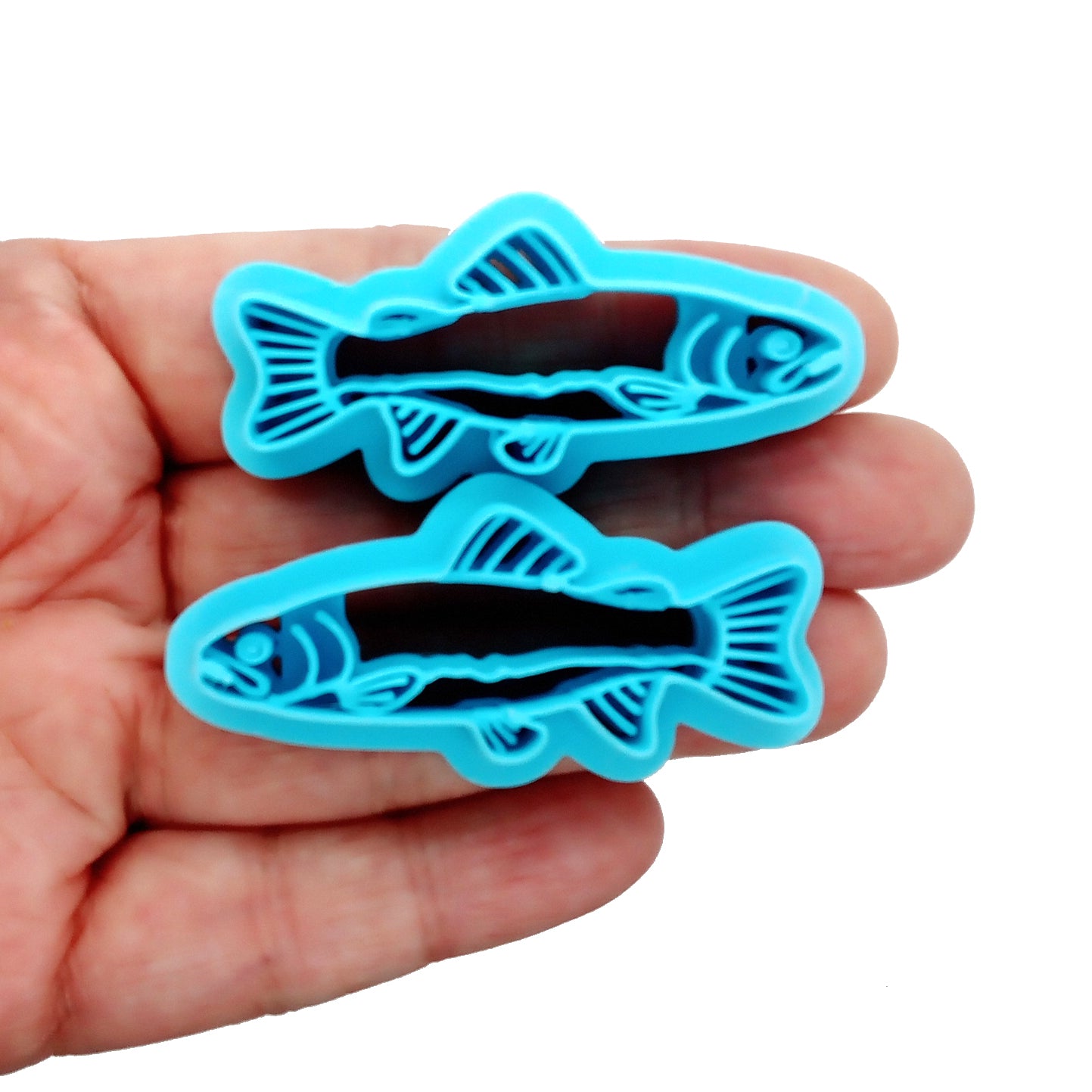 Two blue fish-shaped (salmon) clay cutters in a hand on a white background