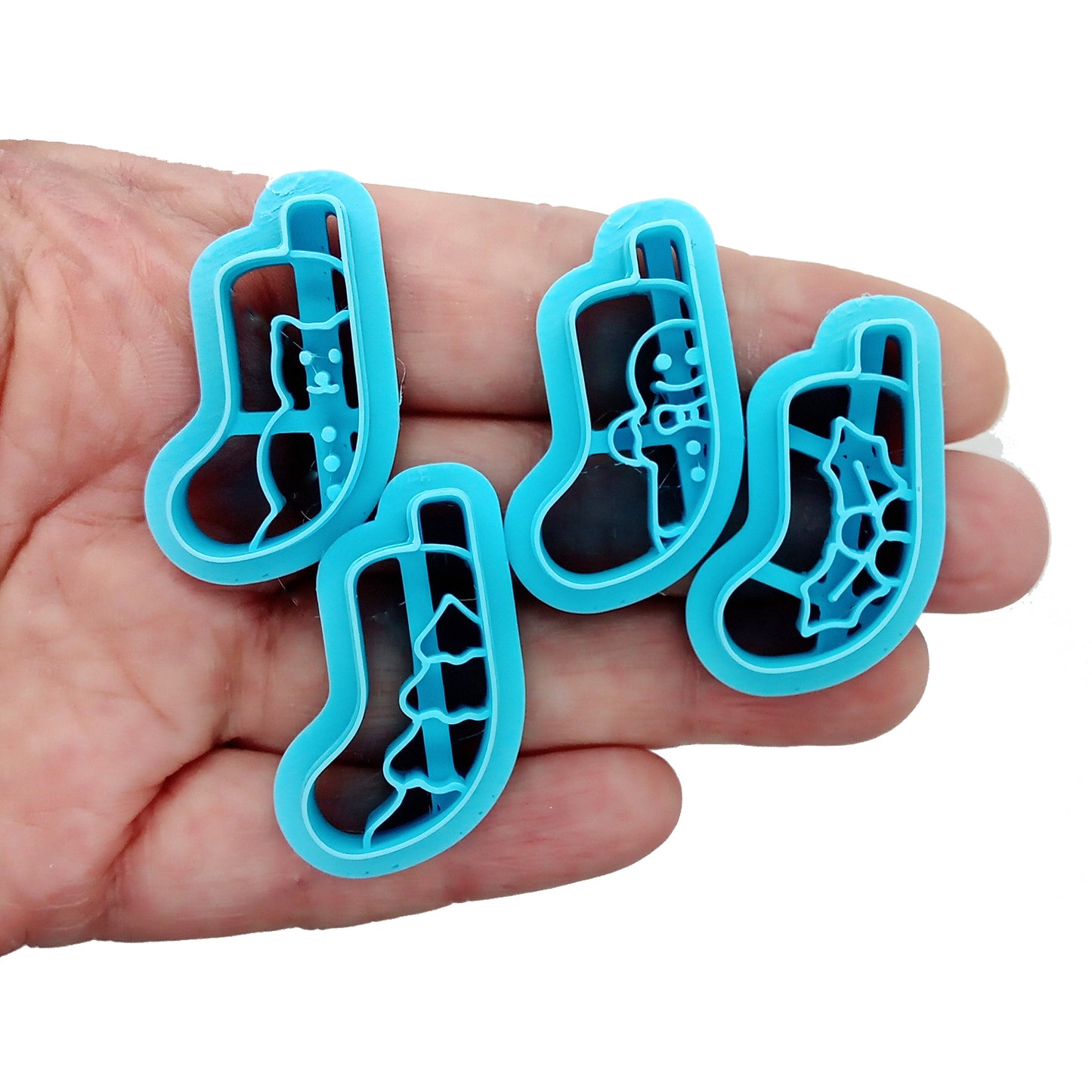 Set of four blue clay cutters, Christmas stocking scenes on a white background held in a hand