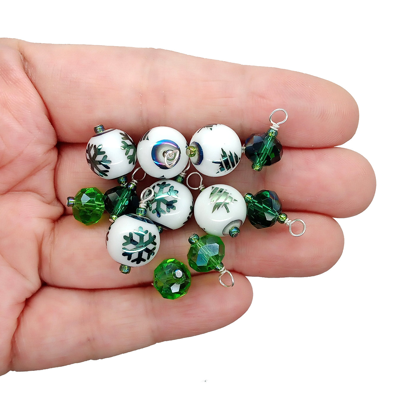 Set of green and white beaded charms in a hand, some with green Christmas trees or snowflakes.