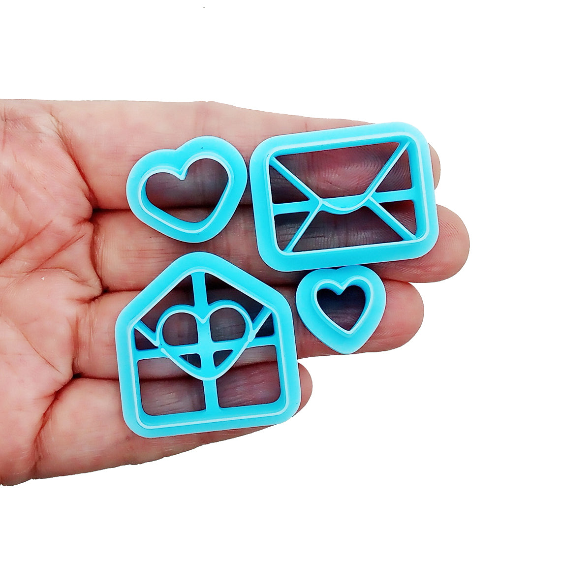 Set of blue clay cutters shaped like hearts and envelopes held in a hand on a white background