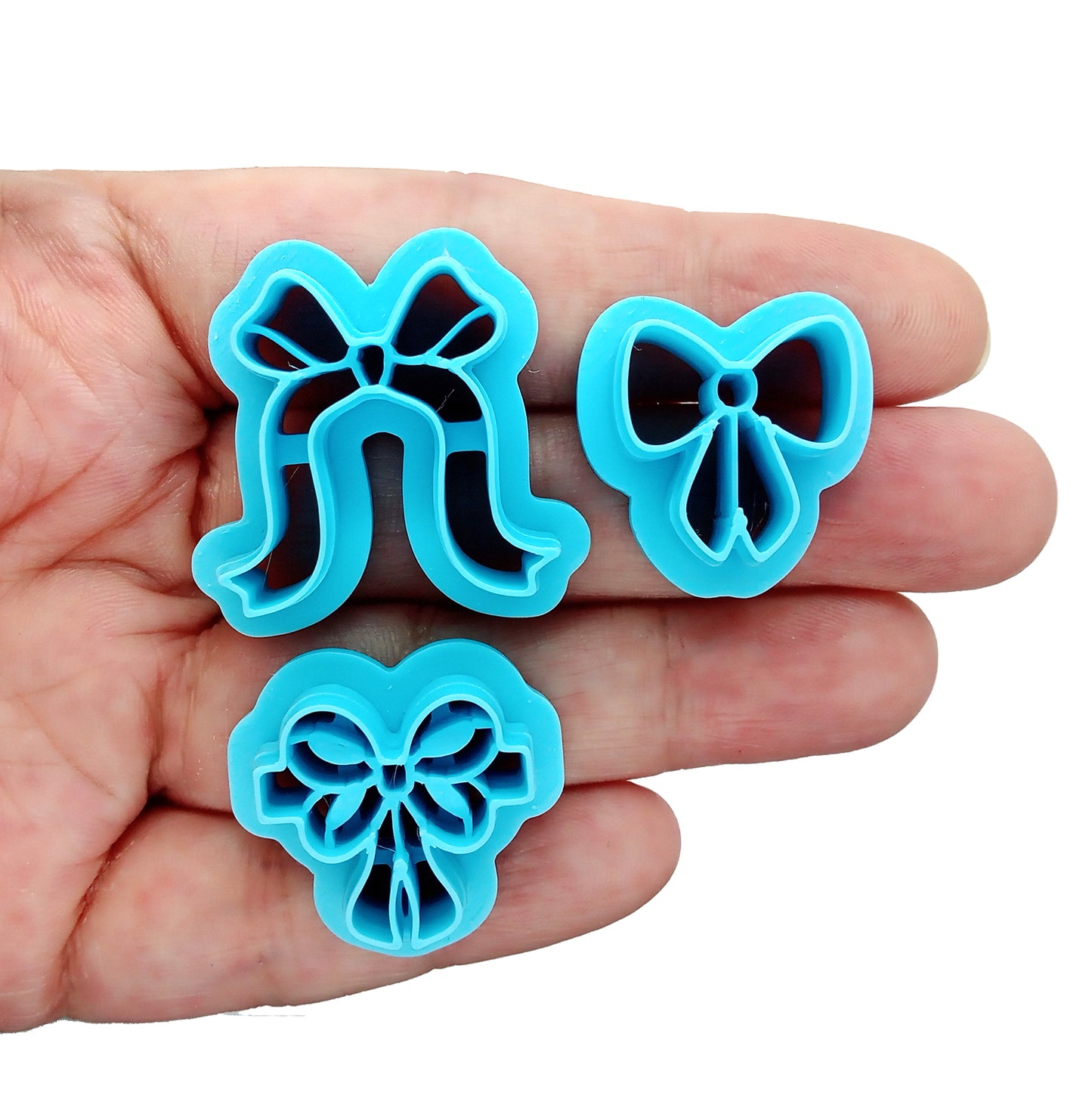 Three blue bow-shaped clay cutters held in a hand against a white background

