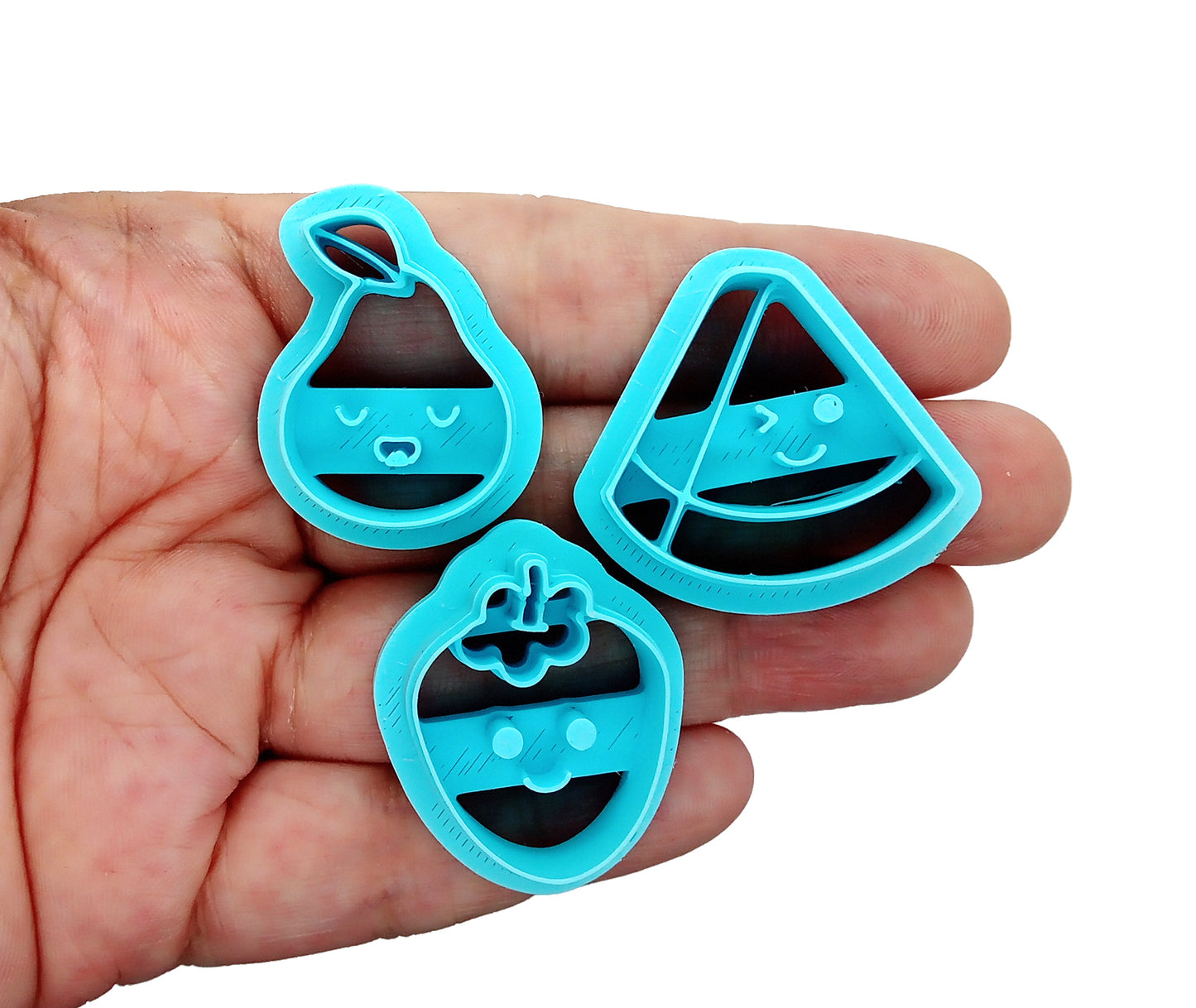 Cute fruit clay cutters: kawaii watermelon, pear and strawberry, held in hand.