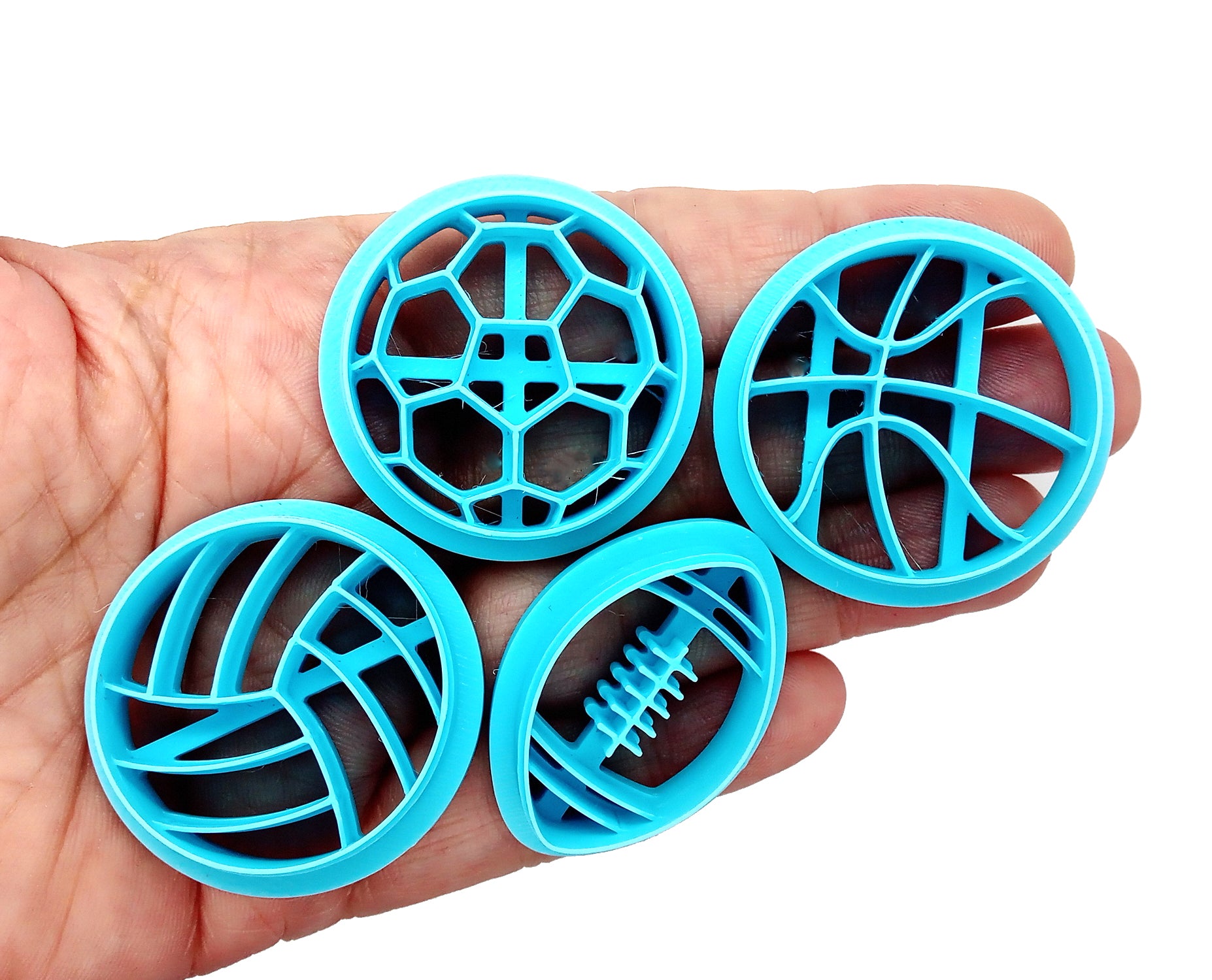 Sports clay cutters: volleyball, soccer ball, basketball and football, shown in hand.