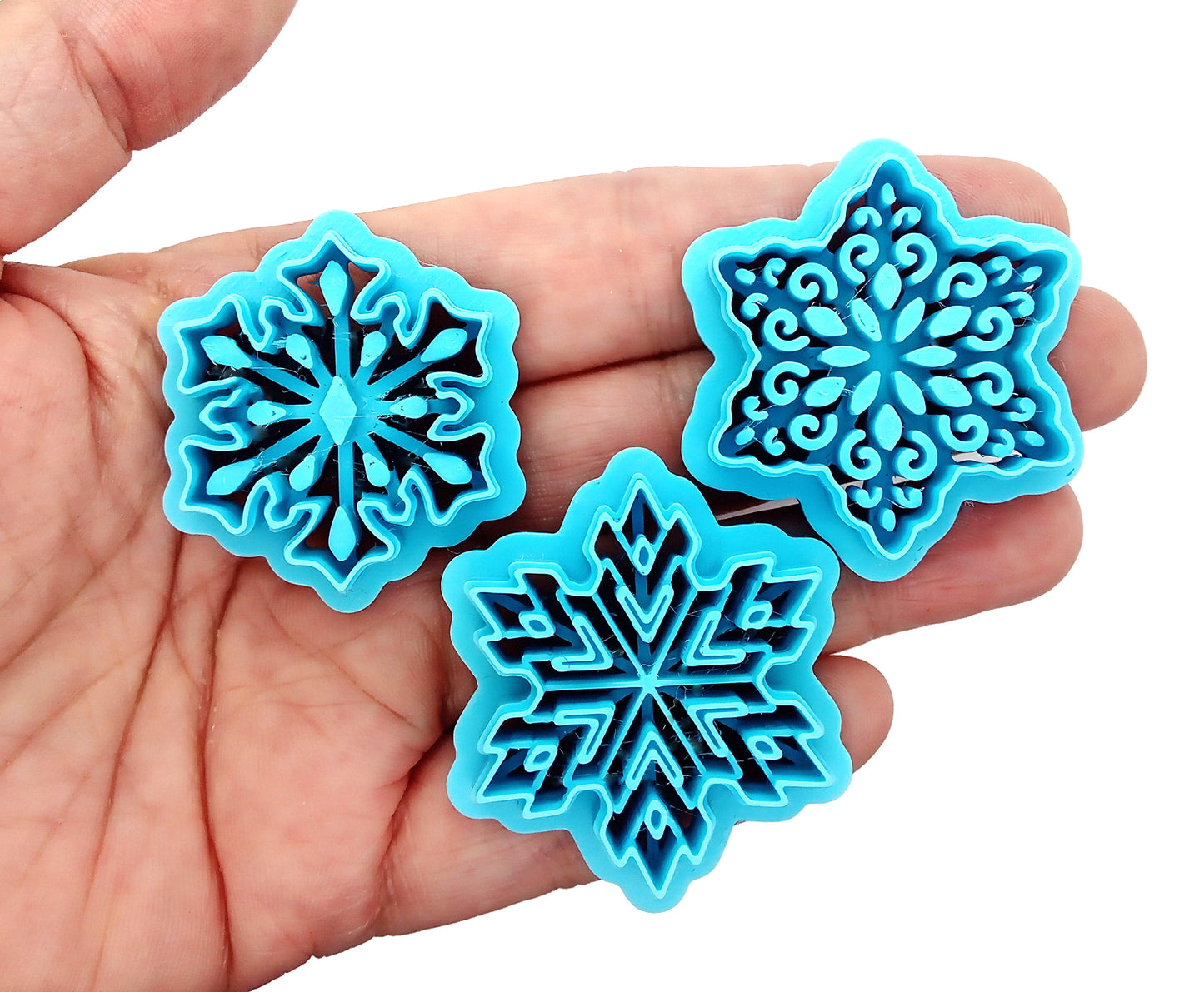 Intricate Snowflake Clay Cutters: Set of 4 displayed in a hand, showcasing sturdy sharp blades and lightweight design.