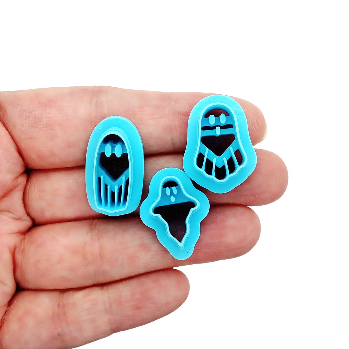 Three blue ghost-shaped clay cutters held in a hand