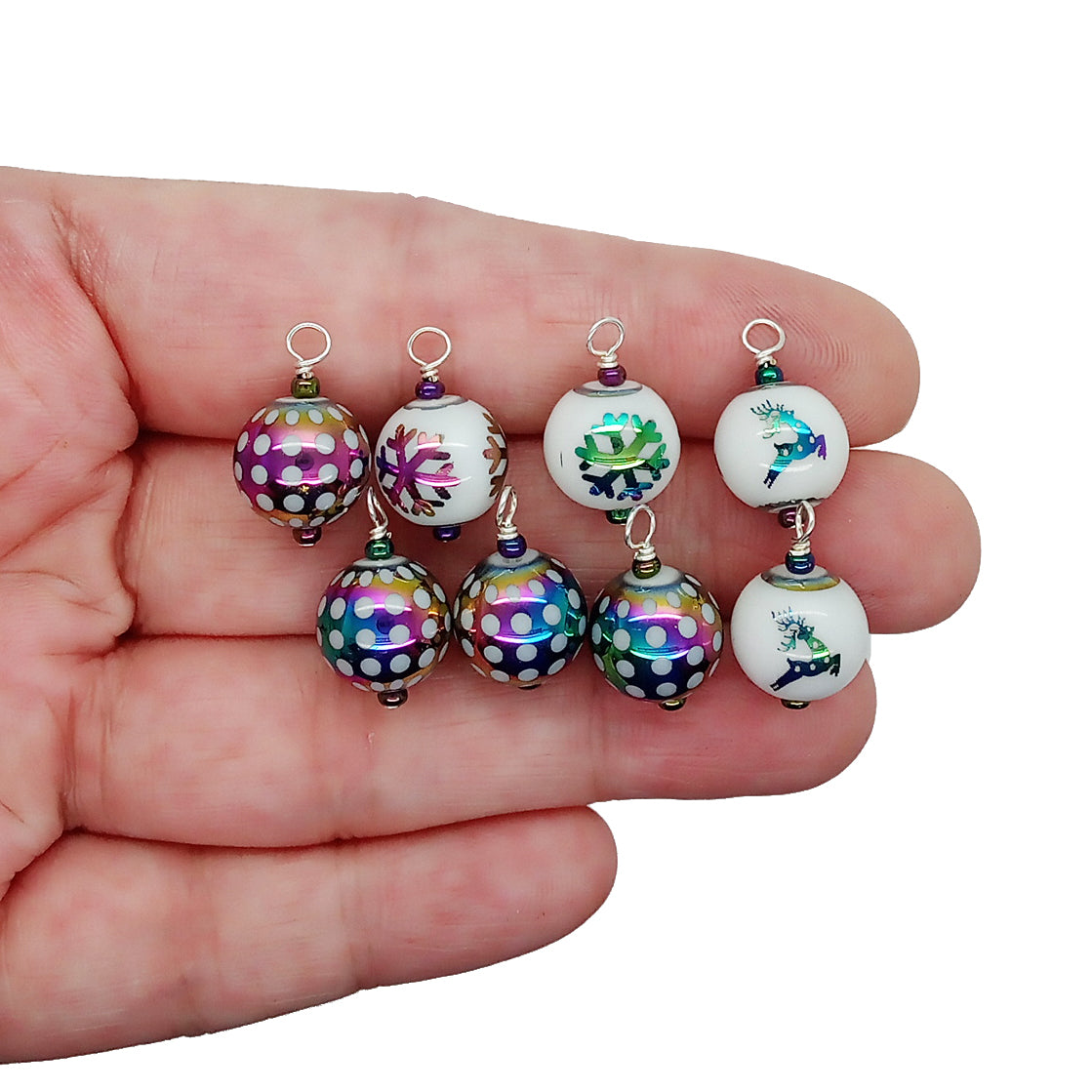 Miniature glass bauble ornaments with rainbow polka dots, snowflakes and reindeer, held in hand.