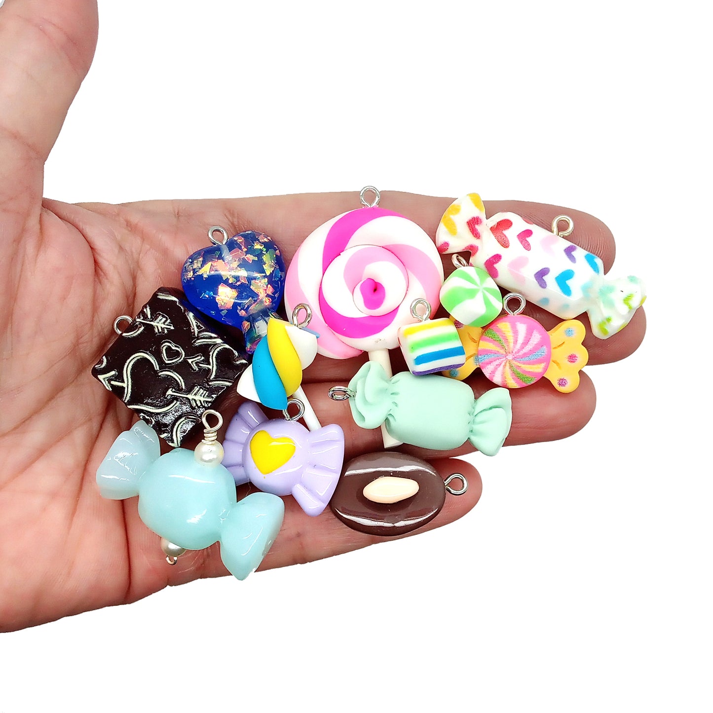 Assorted colorful candy-shaped charms made from resin cabochons, polymer clay and beads, in a hand.