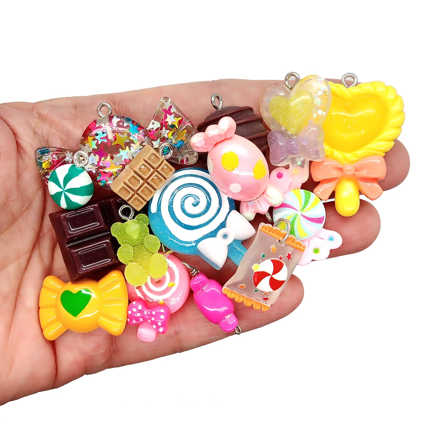 Assorted colorful candy-shaped charms made from resin cabochons, polymer clay and beads, in a hand.