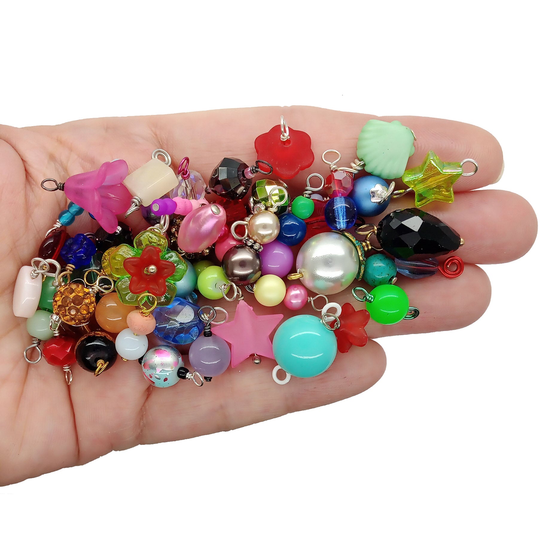 A hand holding a colorful assortment of craft bead charms with small loops, shown against a plain white background.