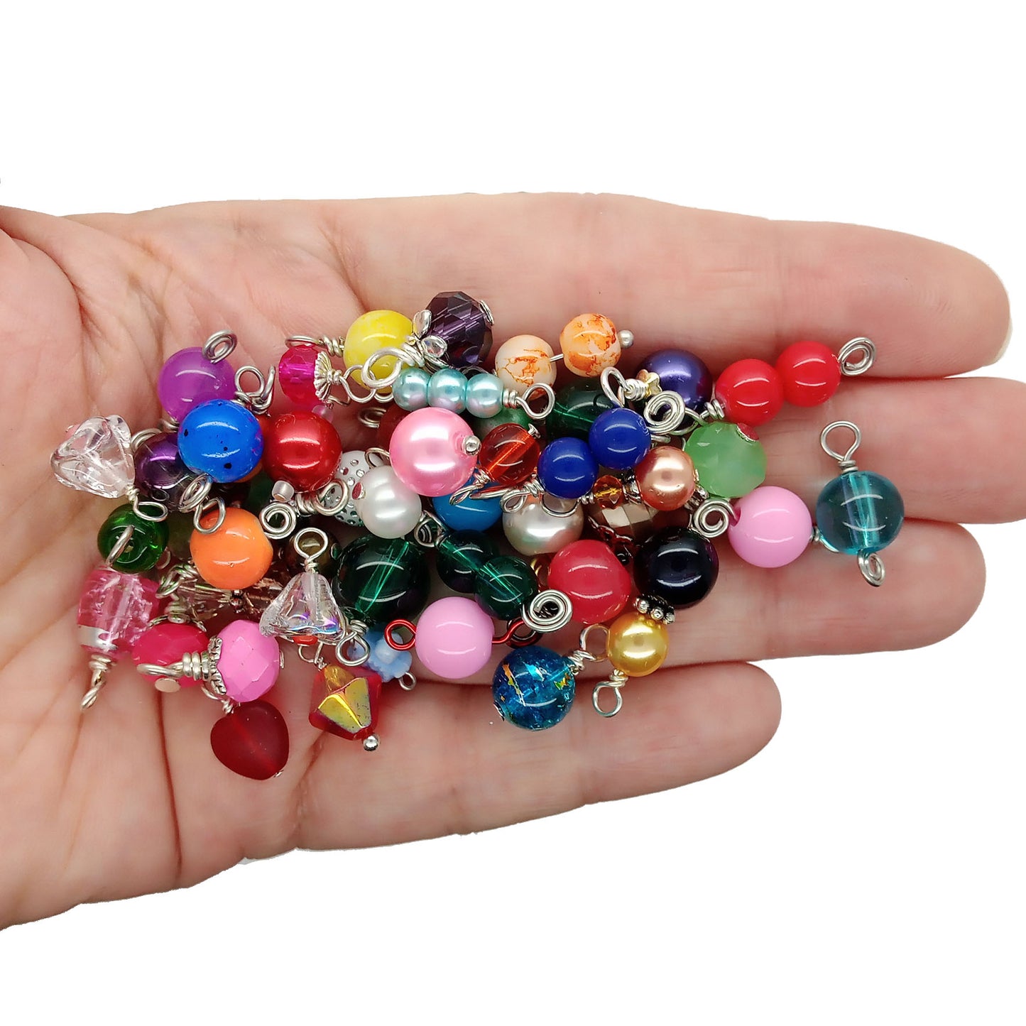 A hand holding a pile of colorful glass bead charms and small dangling charms, photographed against a plain white background.