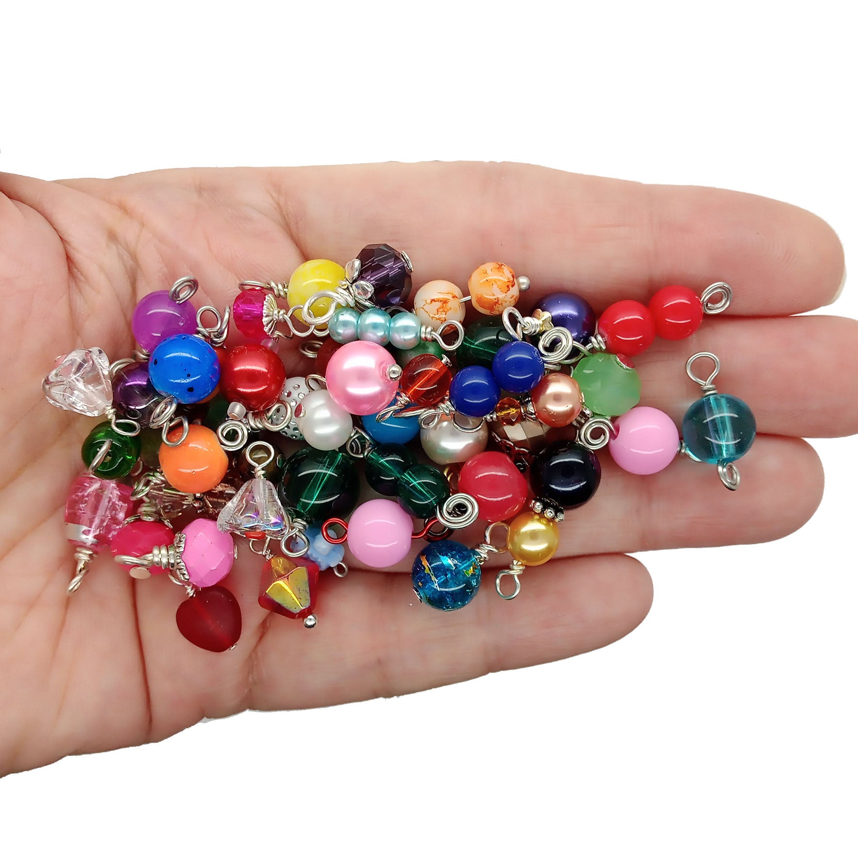 A hand holding a pile of colorful glass bead charms and small dangling charms, photographed against a plain white background.