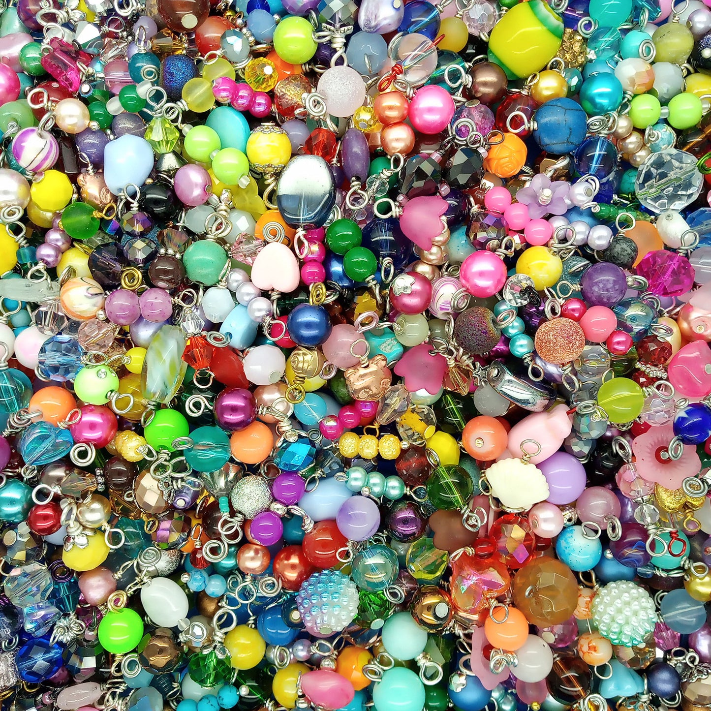 A dense, colorful assortment of craft beads and charms with silver metal loops, filling the entire frame.