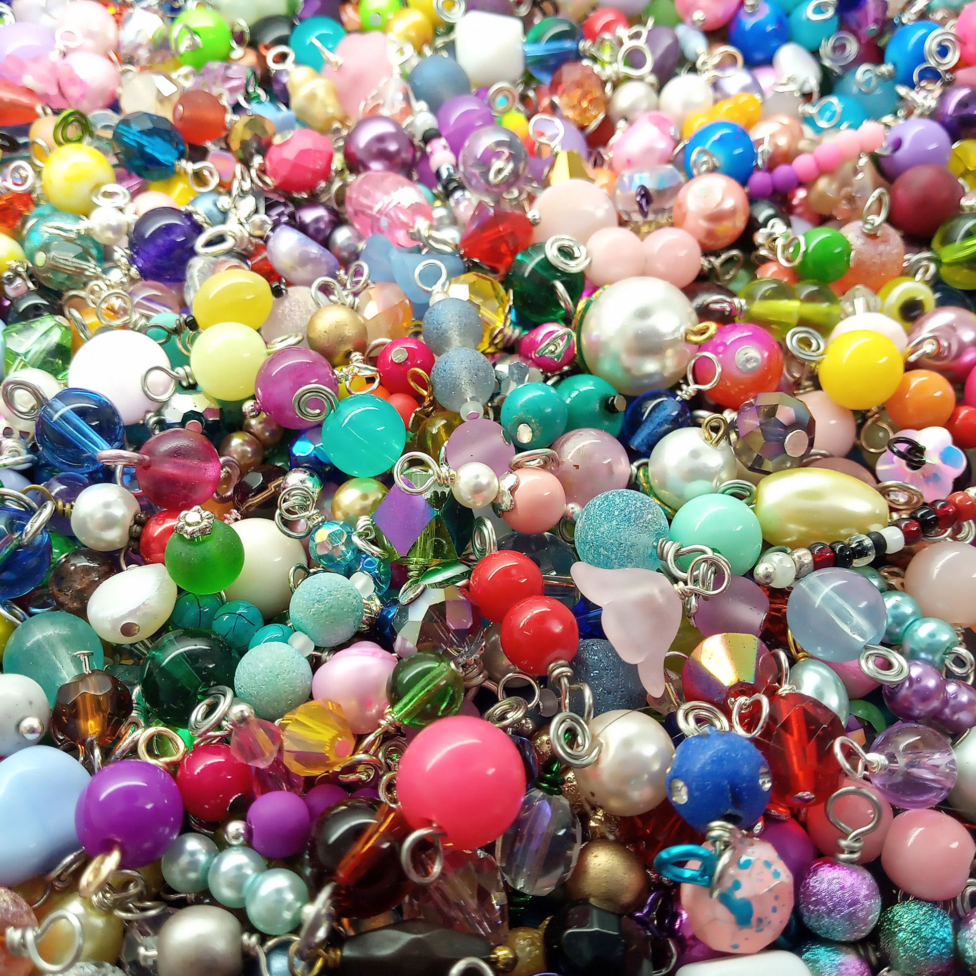 A dense pile of colorful glass bead charms and pendants with silver metal loops, featuring various shapes, sizes, and vibrant colors.