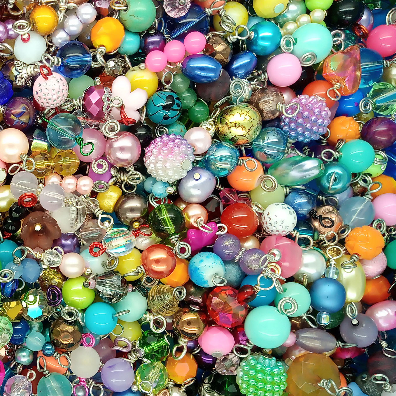 A dense pile of colorful glass and plastic bead dangle charms with various shapes, sizes, and patterns, filling the entire frame.