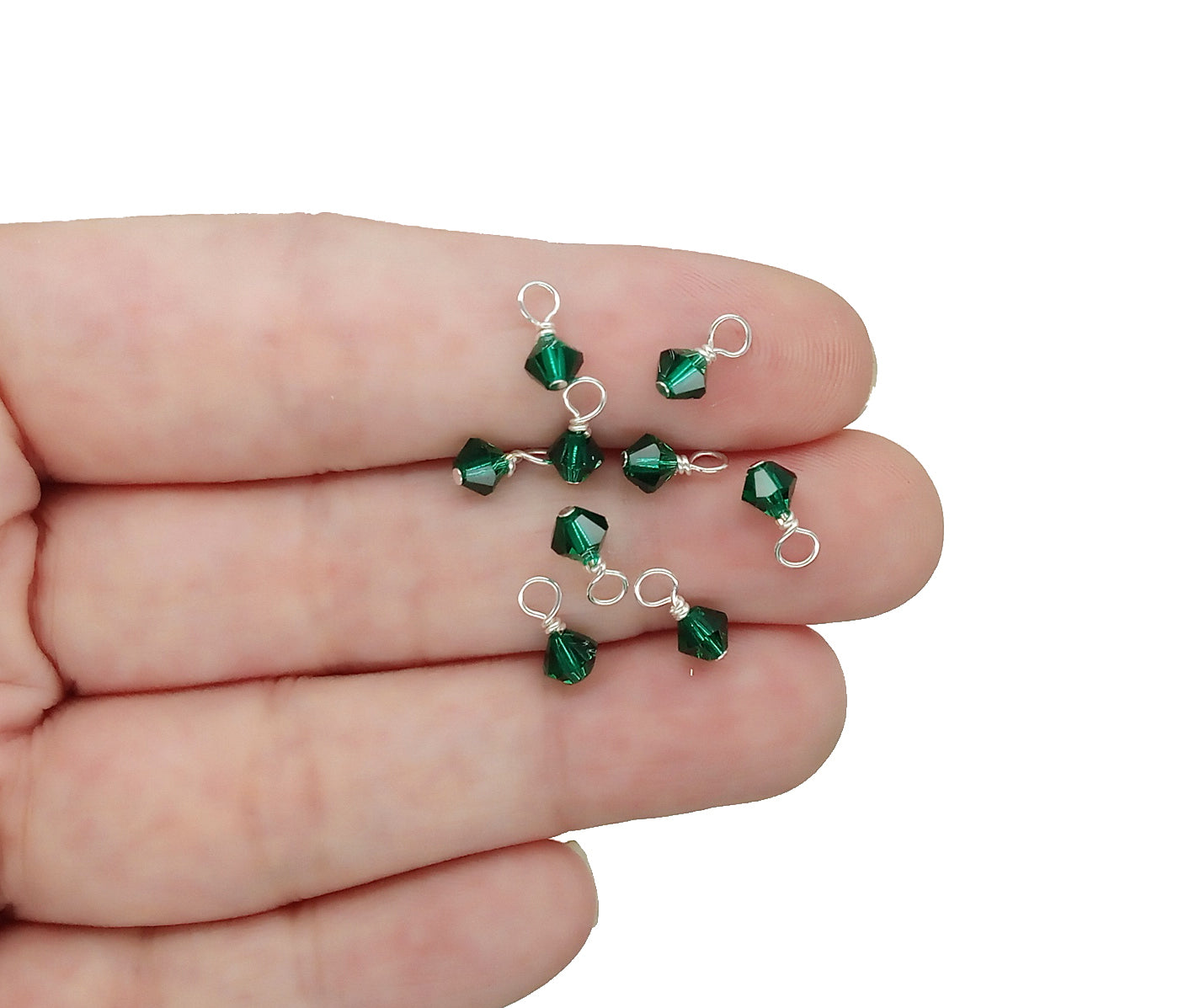 Tiny 4mm crystal bead dangles in emerald are shown on a hand for scale.
