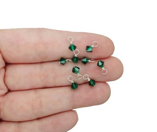 Tiny 4mm crystal bead dangles in emerald are shown on a hand for scale.